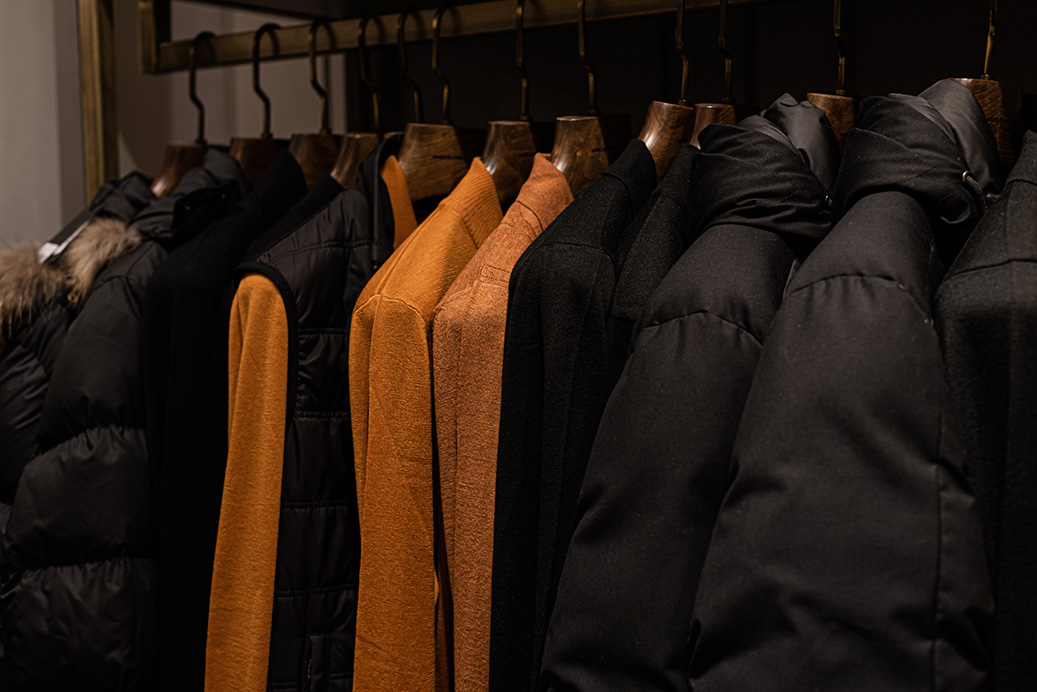 Wardrobe With Men's Clothes In Dark Colors. Jacket, Down Jacket, Shirt. The Clothes Are Neatly Hung On Wooden Hangers