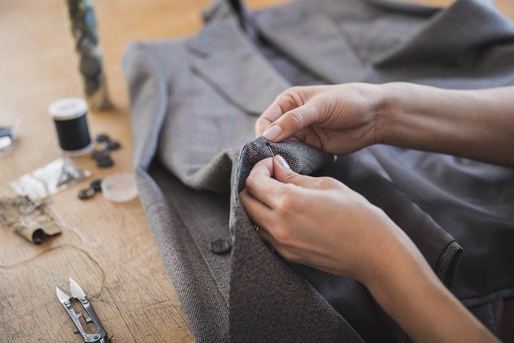 Female Tailor Finishing Off Hand Stitched Button On Jacket